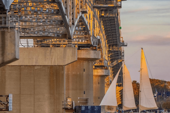 Sailboats near a large steel bridge at sunset.