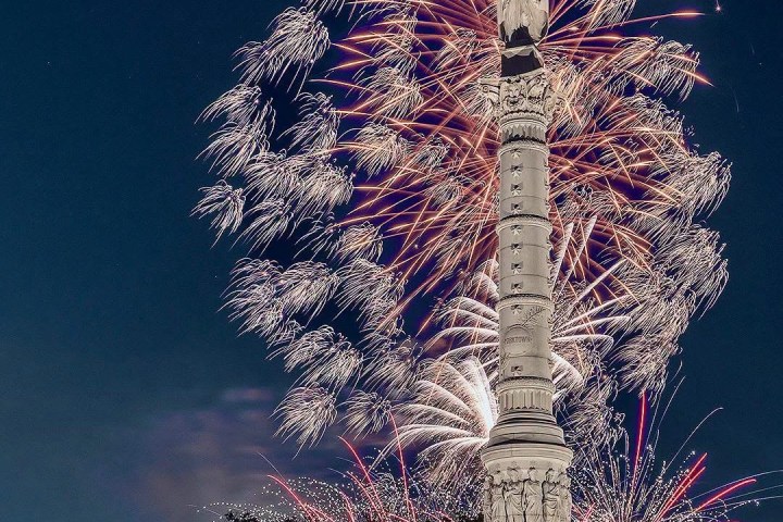 Tall monument with fireworks bursting in the night sky behind it.