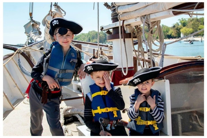 Three children dressed as pirates on a boat, wearing life vests and pirate hats.